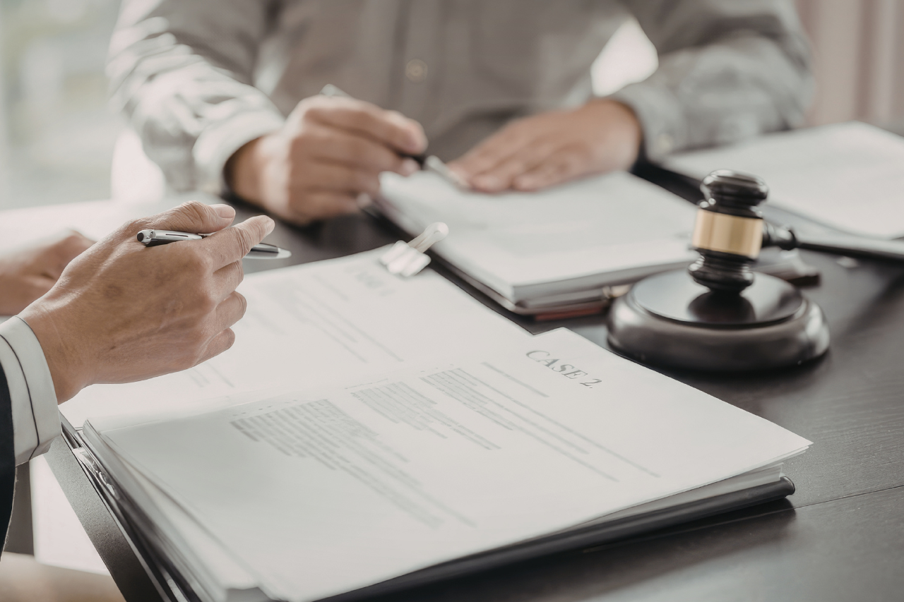 Konsultacja prawna przy dokumentach sprawy z widocznym młotkiem sędziowskim, analiza akt i przygotowanie do postępowania sądowego lub administracyjnego z udziałem prawnika i klienta.